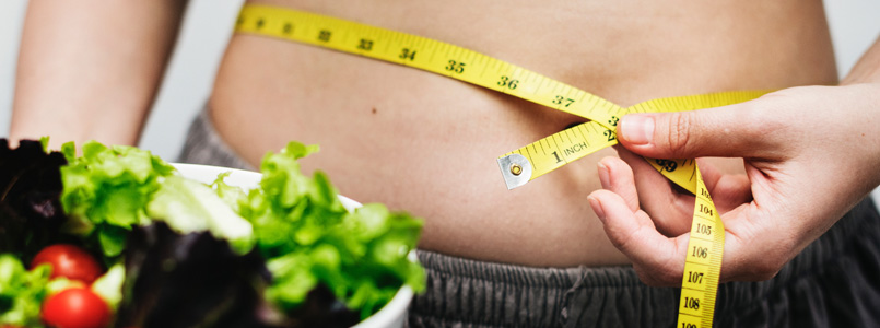 person measuring waist and holding a green salad