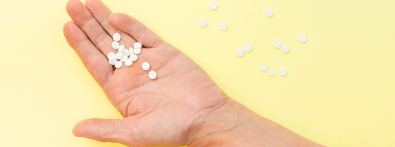 open hand holding white tablets in front of a yellow background