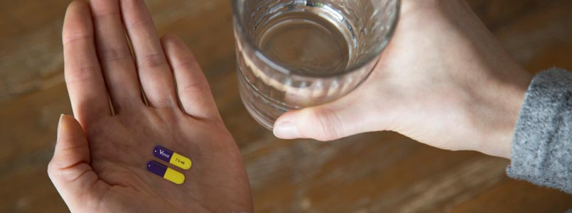 person holding a glass of water in their right hand and two Qsymia weight loss pills in their left hand